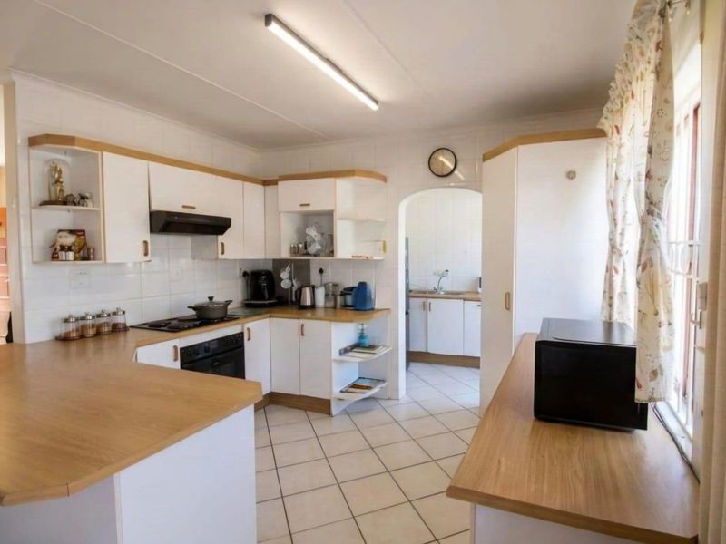 A functional kitchen featuring white cabinetry, wood-look laminate countertops, tiled flooring, and an adjoining scullery area through an arched doorway.
