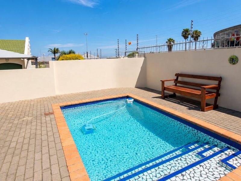 A private outdoor pool area featuring a paved deck, perimeter wall with electric fencing, and integrated pool steps.