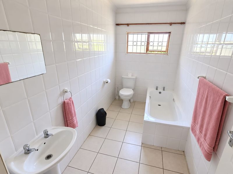 A clean, functional bathroom featuring a pedestal basin, built-in bathtub, and toilet, finished with white wall tiles and neutral floor tiling.