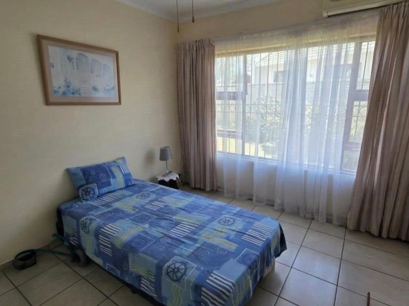 A functional bedroom featuring tiled flooring, an integrated air conditioning unit, and a large window with security bars.