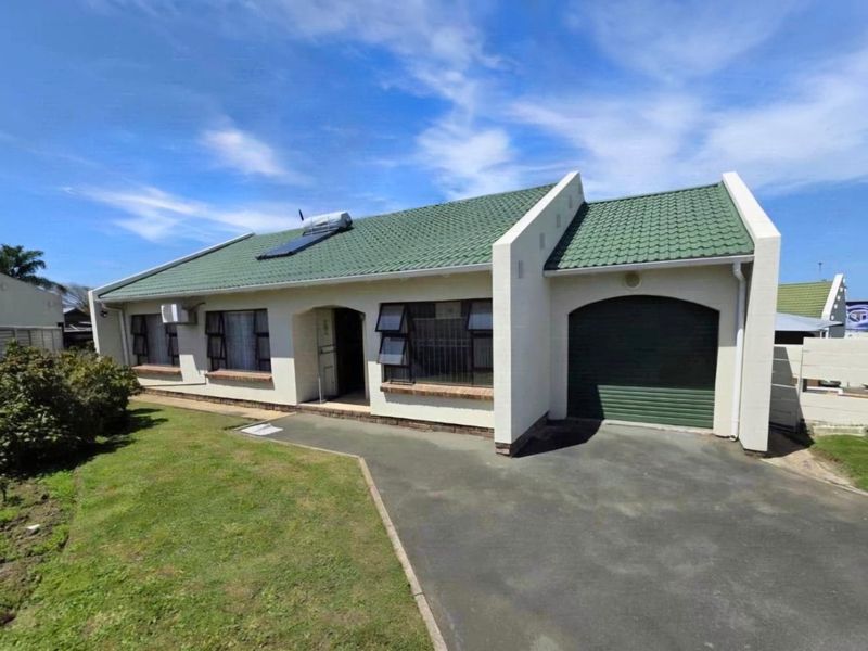 A well-maintained single-story residential home featuring a green tiled roof, integrated garage, paved driveway, and solar water heating system.