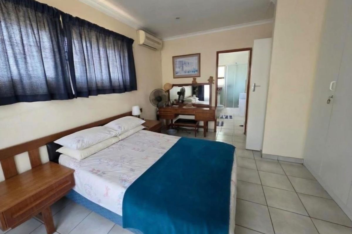 A functional bedroom featuring tiled flooring, built-in cupboards, and an air conditioning unit, with direct access to an en-suite bathroom.