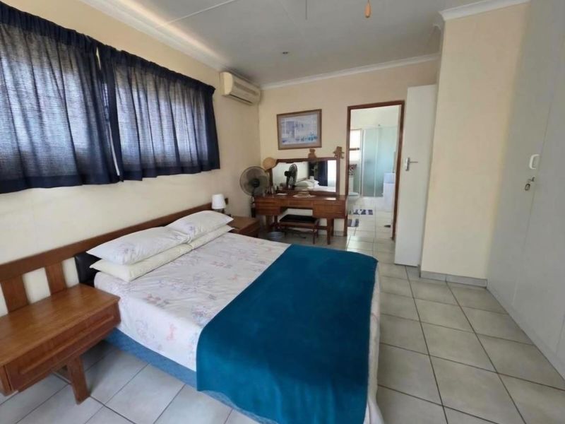 A functional bedroom featuring tiled flooring, built-in cupboards, and an air conditioning unit, with direct access to an en-suite bathroom.