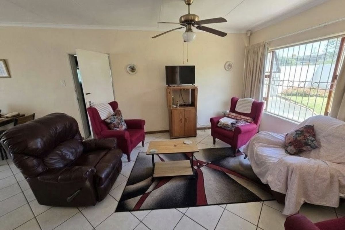 A living room featuring tiled flooring, a ceiling fan, and large windows with security bars, offering a functional space with potential for modernization.