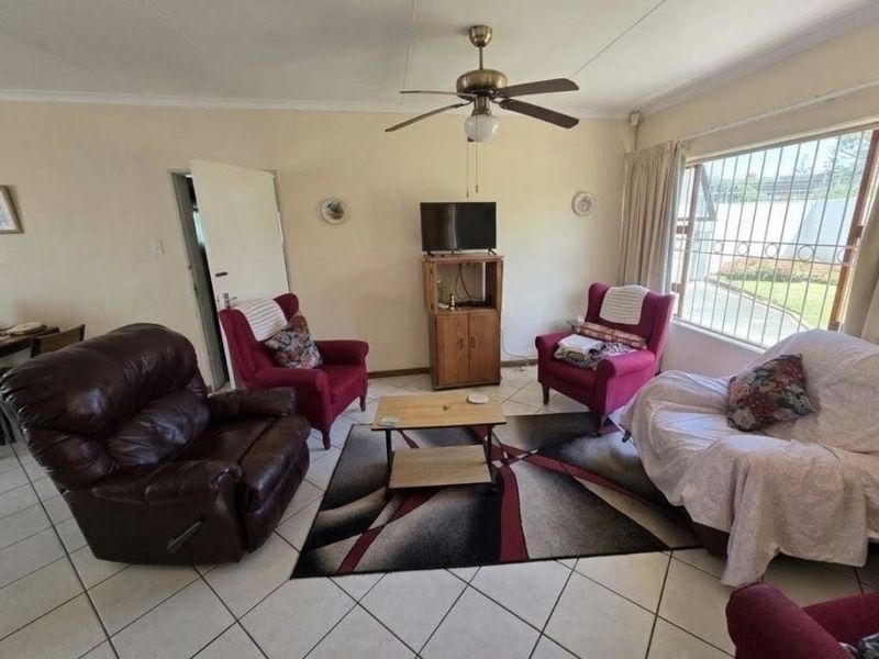 A living room featuring tiled flooring, a ceiling fan, and large windows with security bars, offering a functional space with potential for modernization.