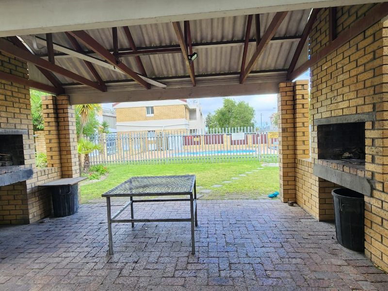 Covered outdoor patio area featuring dual built-in brick braais, paved flooring, and an open-air design overlooking the communal garden and pool area.
