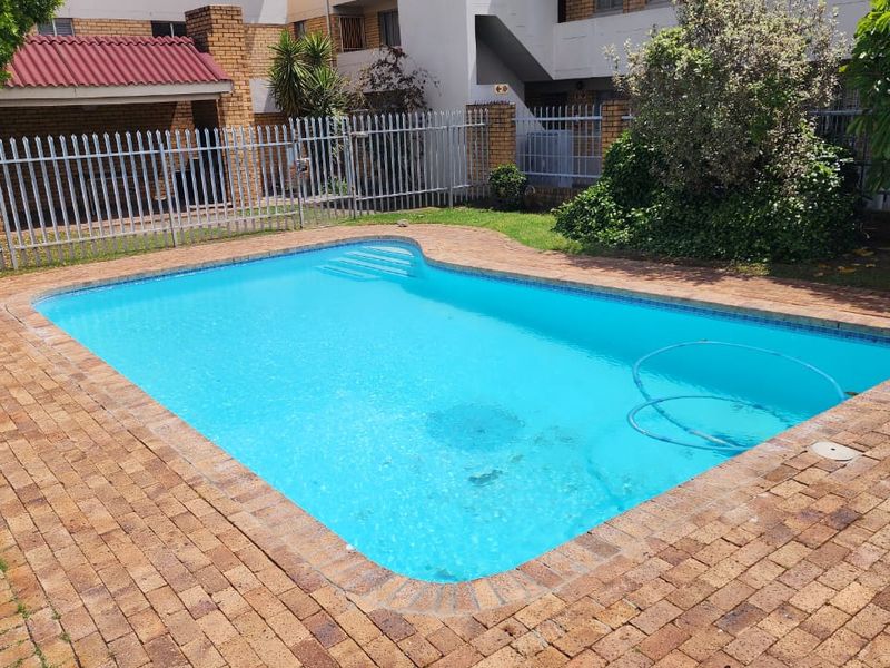 A well-maintained outdoor swimming pool area featuring brick paving surround and secure metal perimeter fencing within a residential complex setting.