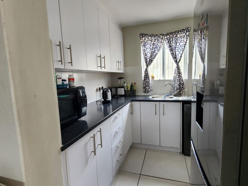 A functional kitchen featuring white cabinetry, black countertops, a stainless steel sink, and tiled flooring, offering a clean and practical workspace.