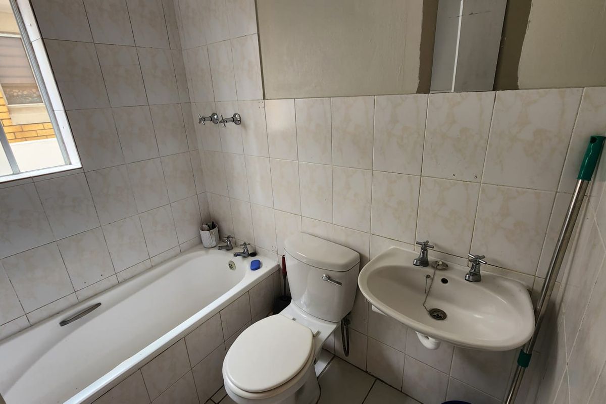A functional bathroom featuring a bathtub, wall-mounted basin, and toilet, finished with tiled walls and flooring. The space is ready for modernization.