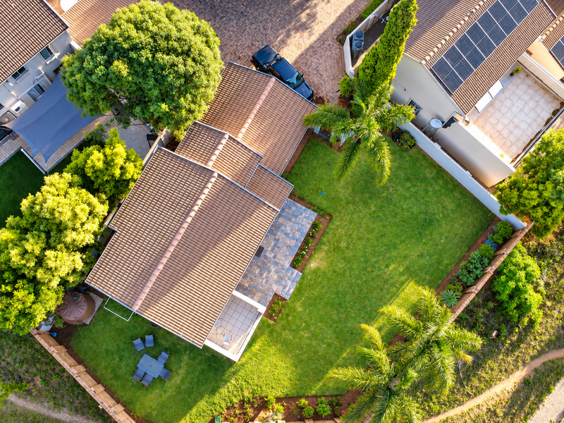 Aerial view of a townhouse property featuring a tiled roof with solar panels, a well-maintained lawn, and a paved patio area.