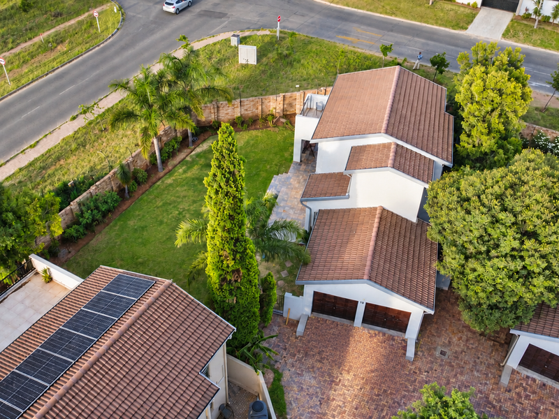 Aerial view of a townhouse property featuring a tiled roof with solar panels, a paved driveway, double garage, and a well-maintained garden.