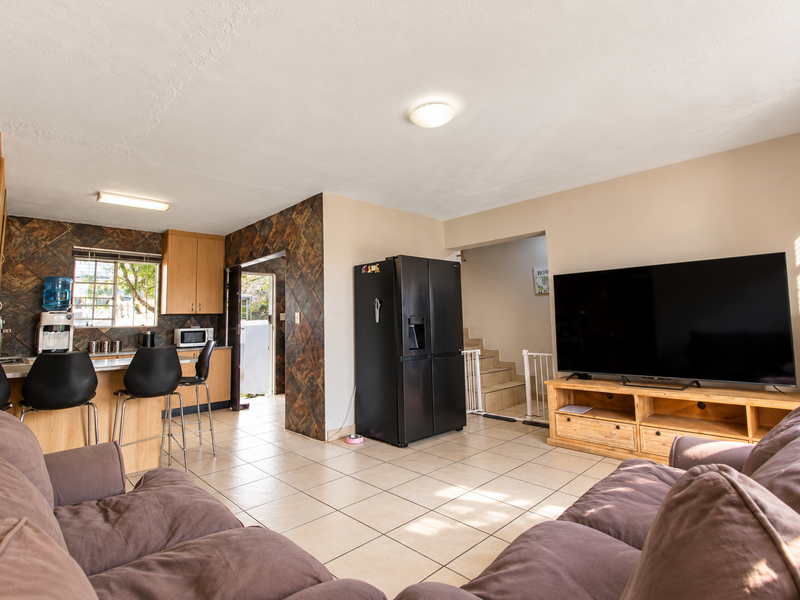 Open-plan living and kitchen area featuring tiled flooring, stone-look wall accents, and a functional kitchen layout with built-in cabinetry.