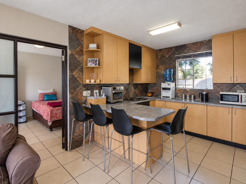 Functional kitchen featuring laminate cabinetry, tiled backsplash, and a built-in breakfast bar, with direct access to an adjacent bedroom.