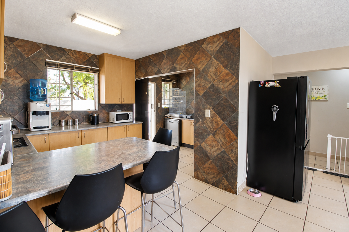 A functional kitchen featuring laminate countertops, built-in cabinetry, and tiled splashbacks, with an adjacent scullery area and tiled flooring throughout.