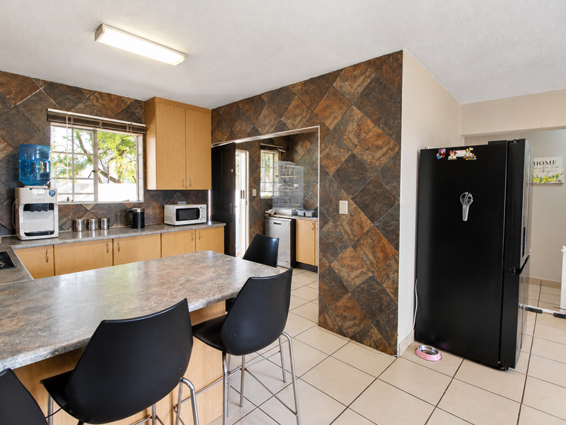 A functional kitchen featuring laminate countertops, built-in cabinetry, and tiled splashbacks, with an adjacent scullery area and tiled flooring throughout.