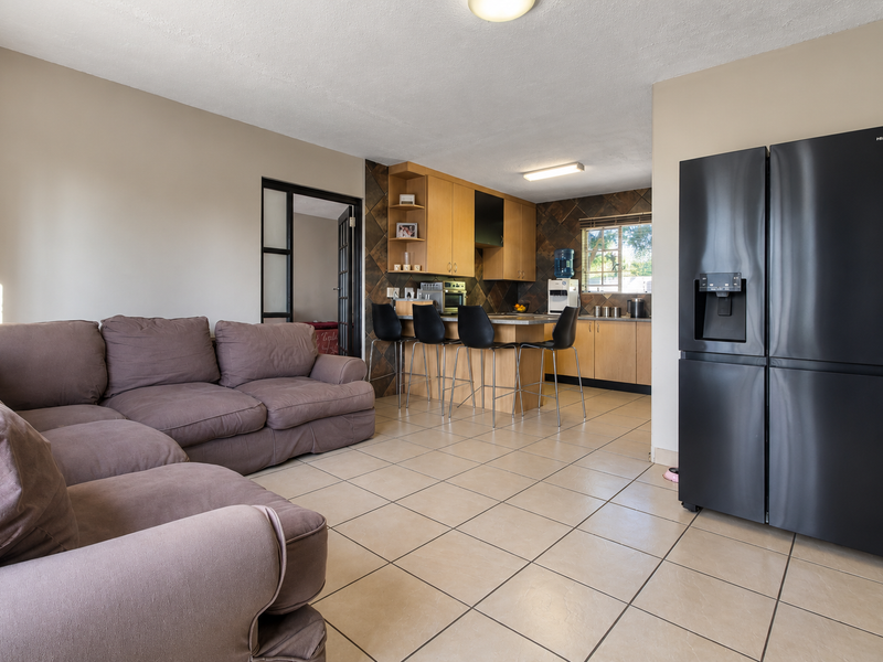 Open plan living and kitchen area featuring ceramic floor tiles, wooden cabinetry, a breakfast bar, and direct access to an adjacent room via french doors.