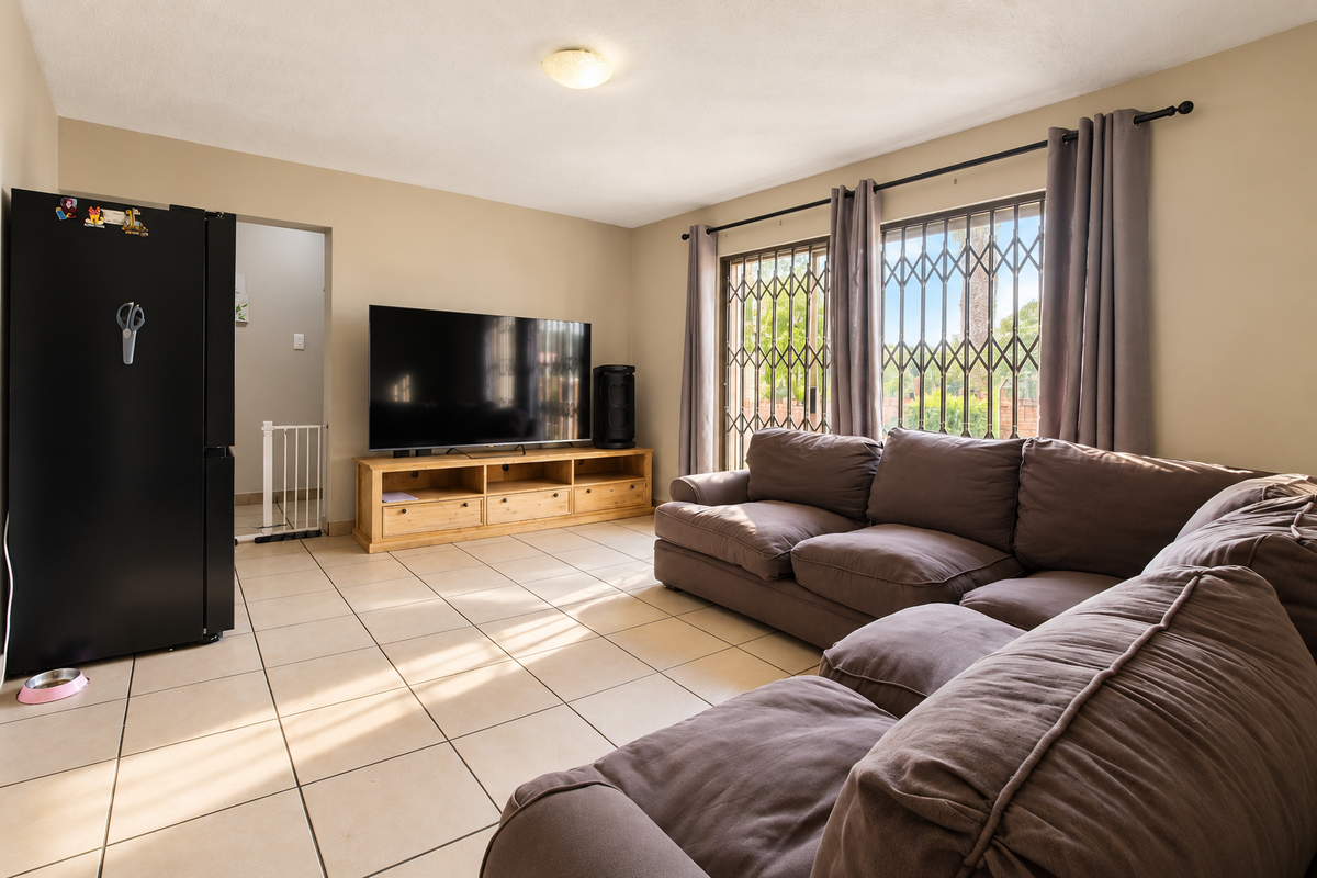 A spacious living room featuring neutral ceramic floor tiles, large sliding glass doors with security gates, and direct access to an adjacent area.