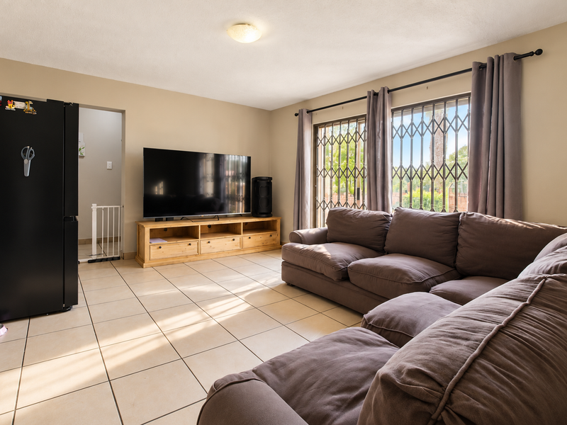 A spacious living room featuring neutral ceramic floor tiles, large sliding glass doors with security gates, and direct access to an adjacent area.