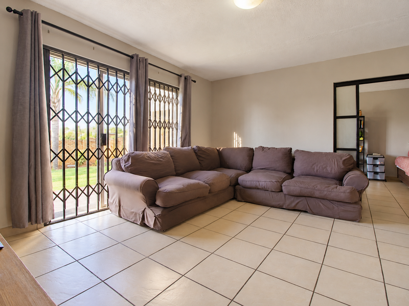 Spacious living room featuring neutral tiled flooring and a sliding glass door with security gate providing access to the garden.