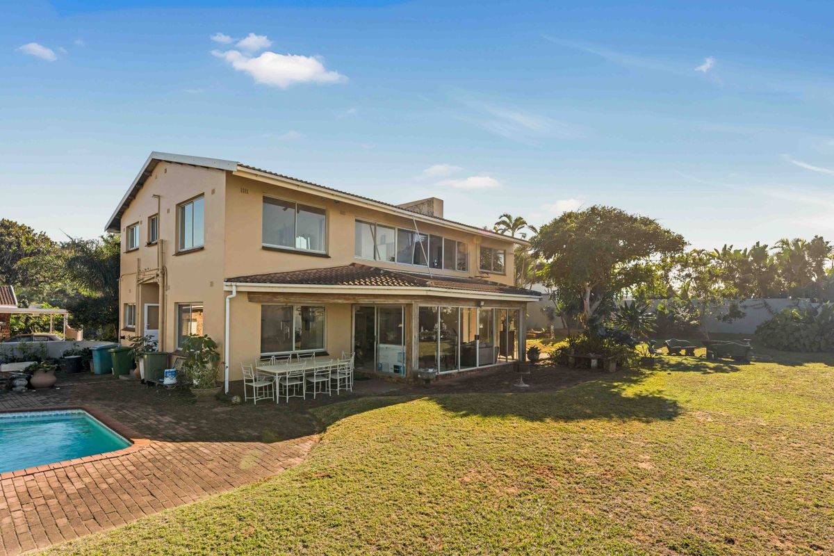 Rear view of the house featuring a swimming pool, brick paved patio area, and a spacious garden with established trees.