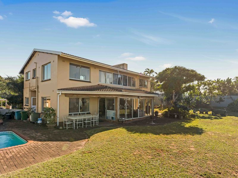 Rear view of the house featuring a swimming pool, brick paved patio area, and a spacious garden with established trees.