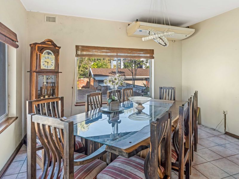 A dining room featuring tiled flooring, large windows providing natural light, and a wall-mounted air conditioning unit.