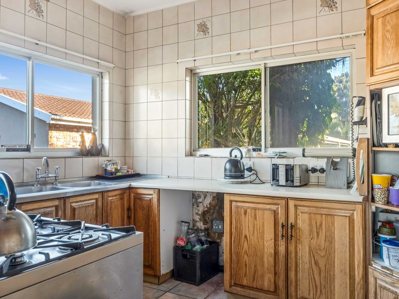 A dated kitchen featuring wooden cabinetry, a gas hob, and tiled splashbacks, requiring cosmetic updates to modernize the space.