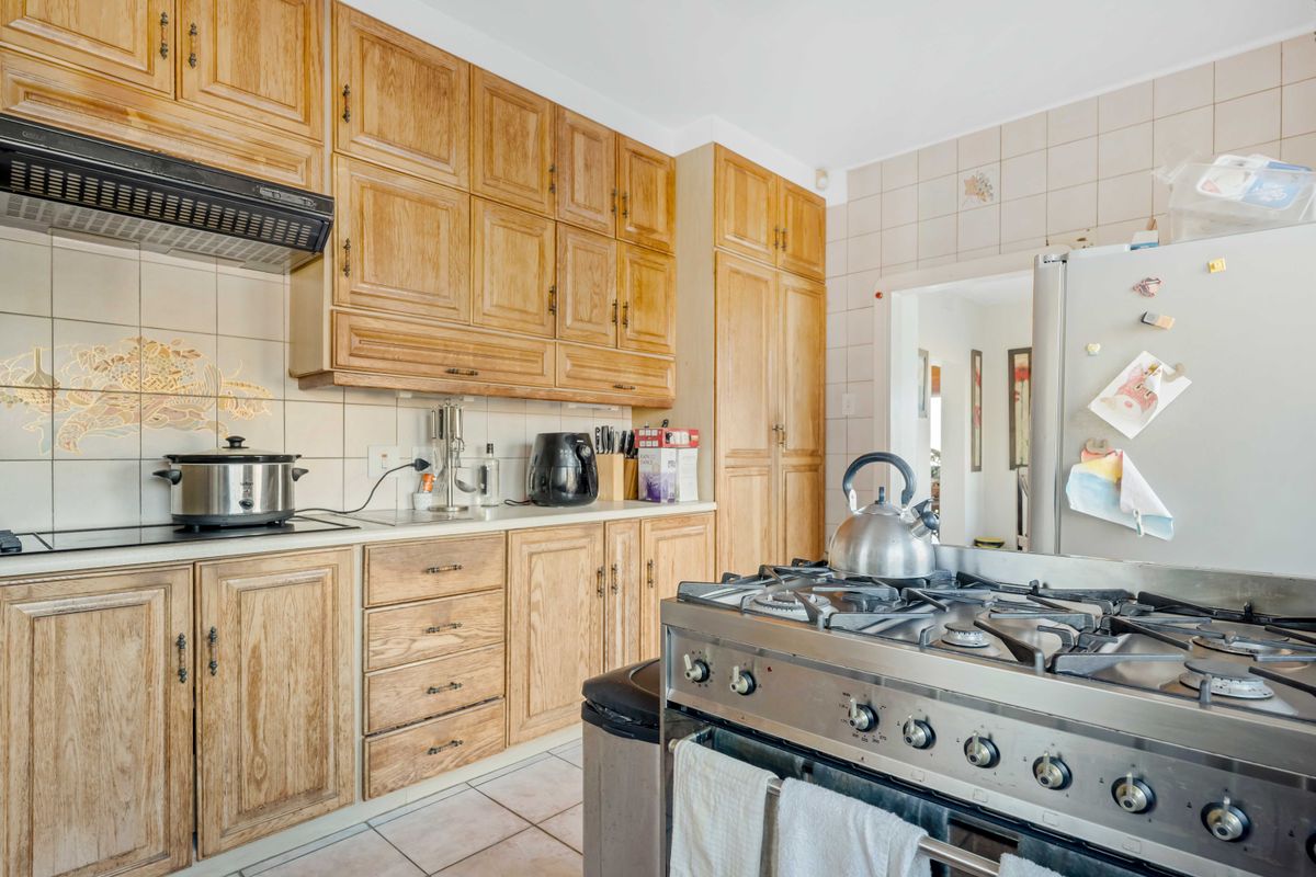 A functional kitchen featuring traditional wooden cabinetry, a gas stove, extractor fan, and tiled backsplash, offering a classic layout with ample storage space.