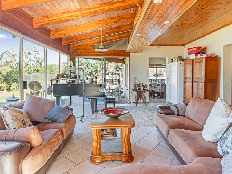Spacious living area featuring exposed timber beam ceilings, tiled flooring, and large sliding glass doors providing ample natural light and garden views.