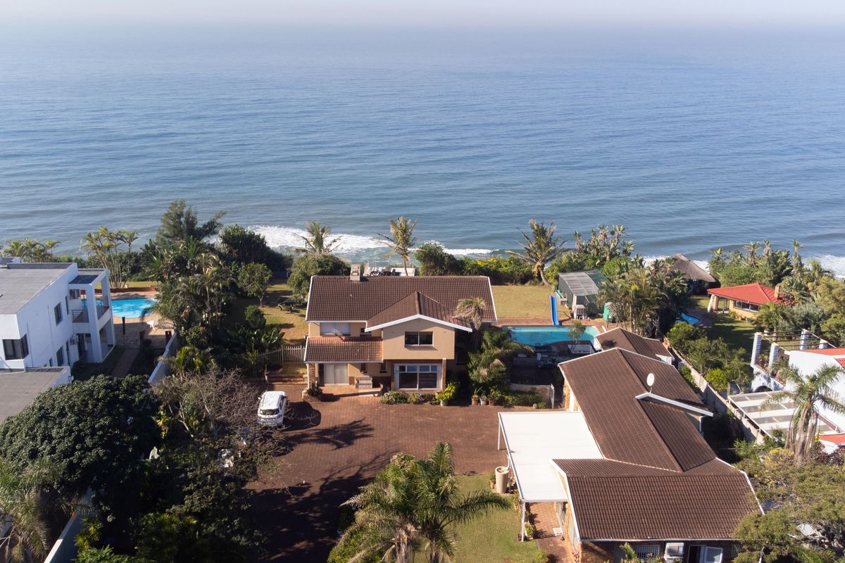 Aerial view of a coastal residential property featuring a swimming pool, expansive paved driveway, and direct ocean views.