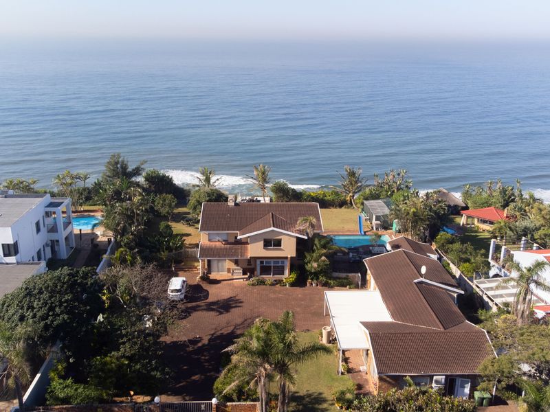 Aerial view of a coastal residential property featuring a swimming pool, expansive paved driveway, and direct ocean views.