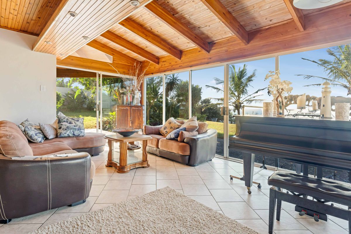 Spacious living area featuring a warm timber-beamed ceiling, tiled flooring, and expansive sliding glass doors that provide abundant natural light and garden views.