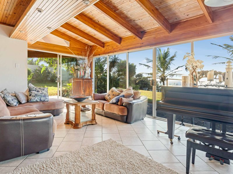 Spacious living area featuring a warm timber-beamed ceiling, tiled flooring, and expansive sliding glass doors that provide abundant natural light and garden views.