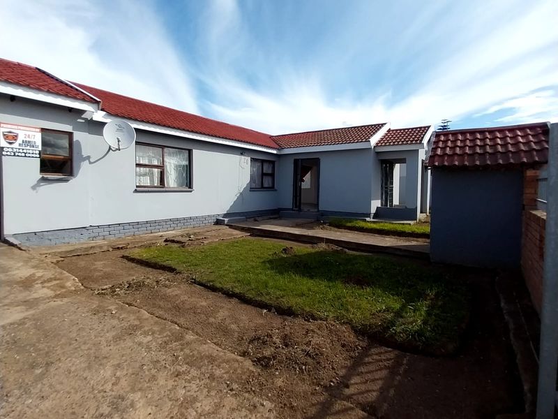 Rear view of the property featuring a tiled roof, concrete driveway, and an enclosed yard area with ongoing landscaping work.