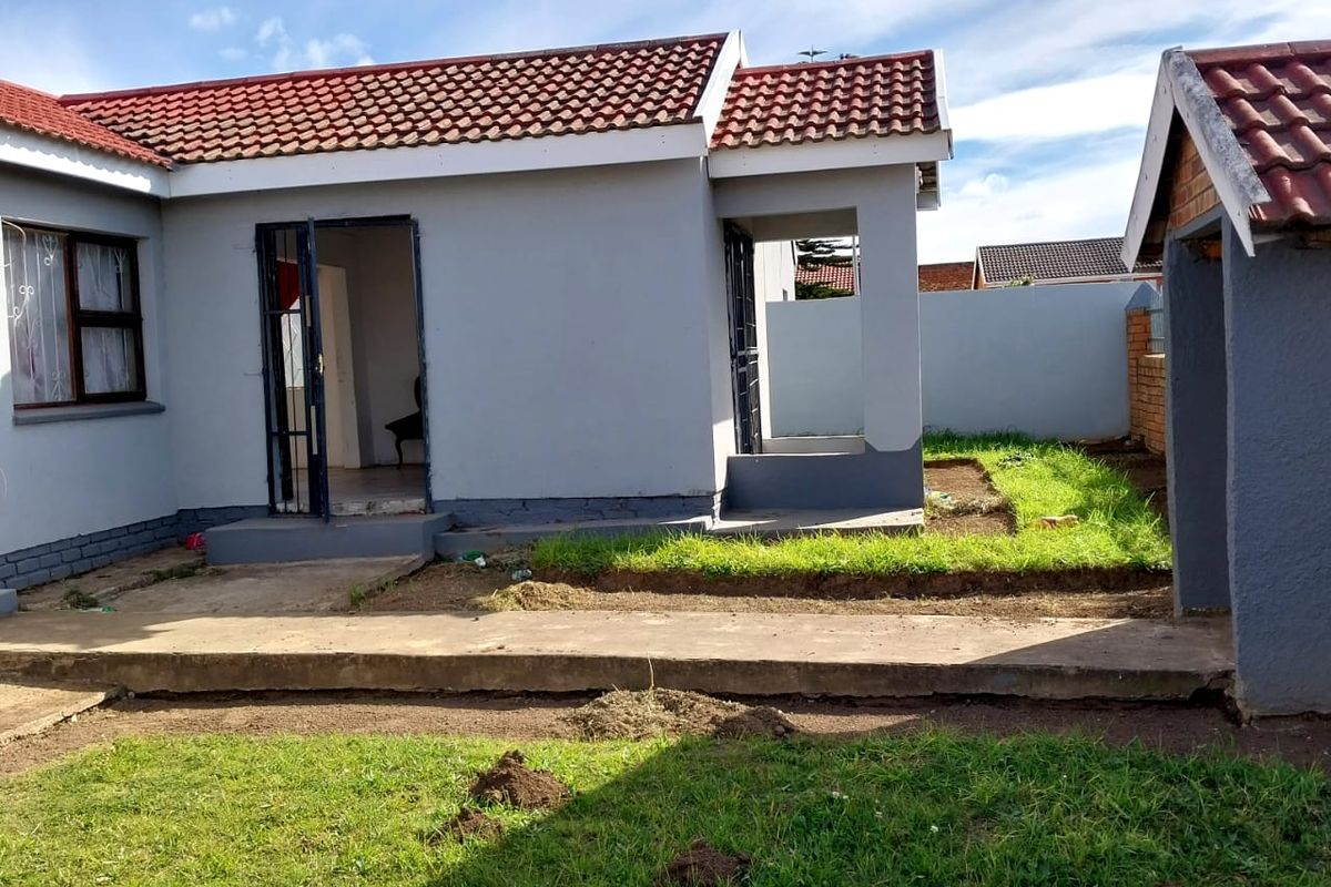 Rear view of the house featuring a concrete patio, tiled roof, and a surrounding boundary wall with an established garden area.