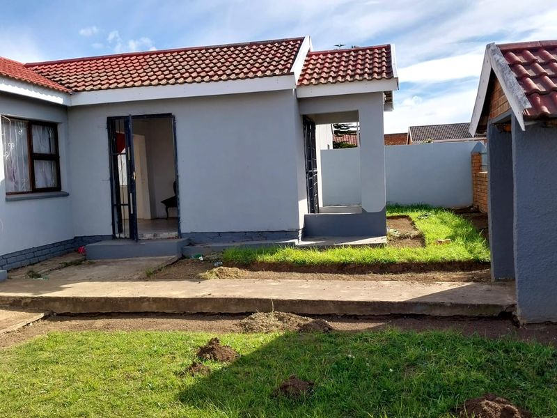 Rear view of the house featuring a concrete patio, tiled roof, and a surrounding boundary wall with an established garden area.