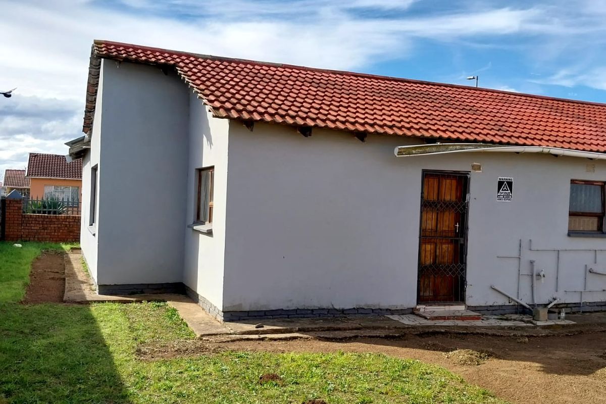 Rear view of the property featuring a tiled roof, security gate, and an unfinished garden area with exposed external plumbing.