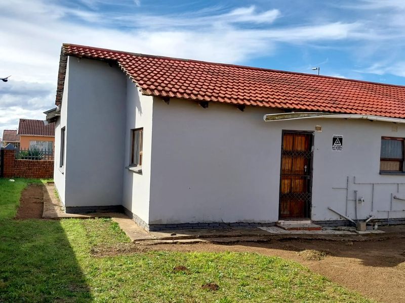 Rear view of the property featuring a tiled roof, security gate, and an unfinished garden area with exposed external plumbing.