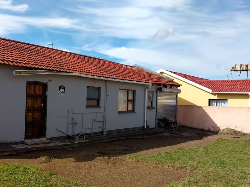 Rear view of the property featuring a tiled roof, roller shutter garage door, and an expansive backyard area requiring landscaping.