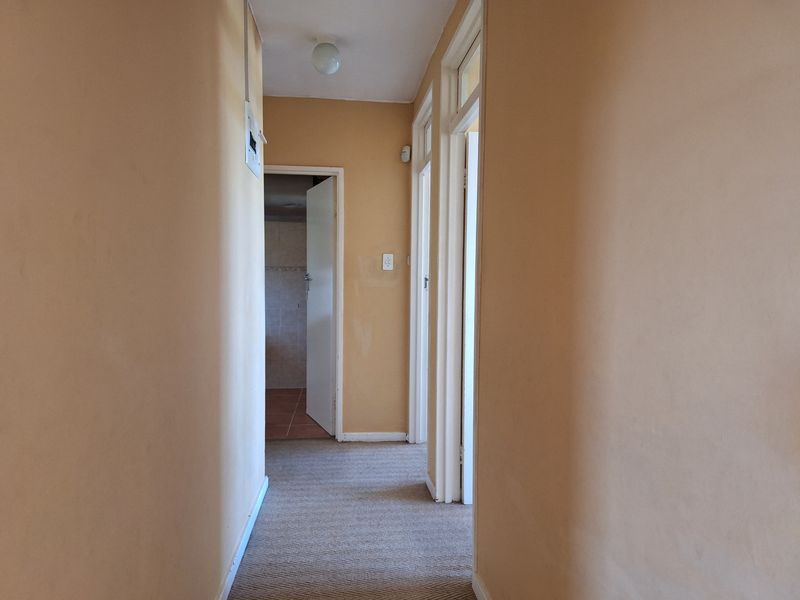 A functional hallway connecting multiple rooms, featuring neutral wall paint, carpeted flooring, and access to a tiled bathroom area.
