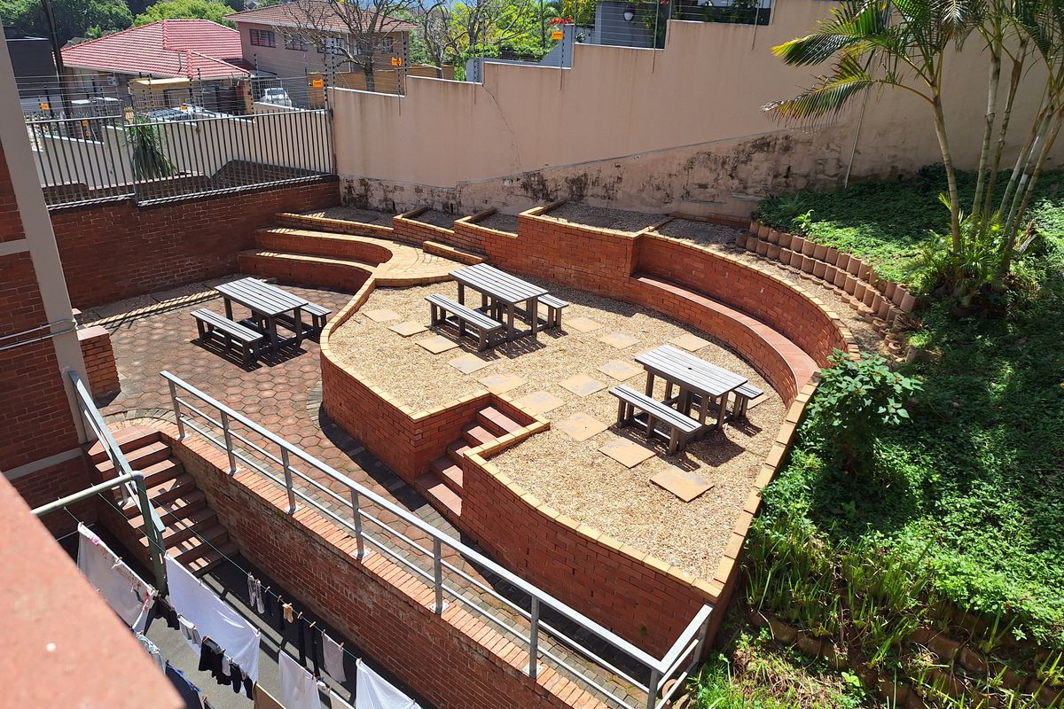 A multi-level outdoor terrace featuring brick retaining walls, paved and gravel sections, and metal railings, providing a communal outdoor space.
