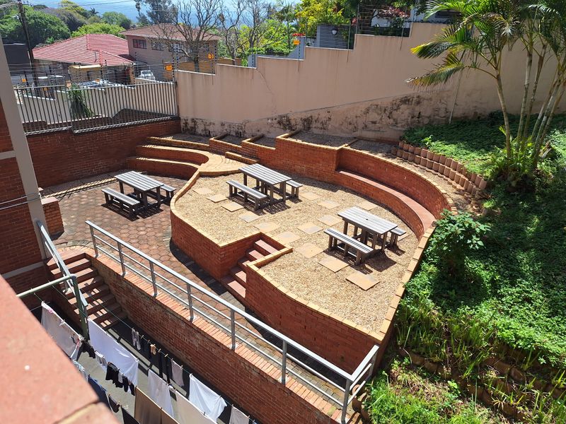 A multi-level outdoor terrace featuring brick retaining walls, paved and gravel sections, and metal railings, providing a communal outdoor space.
