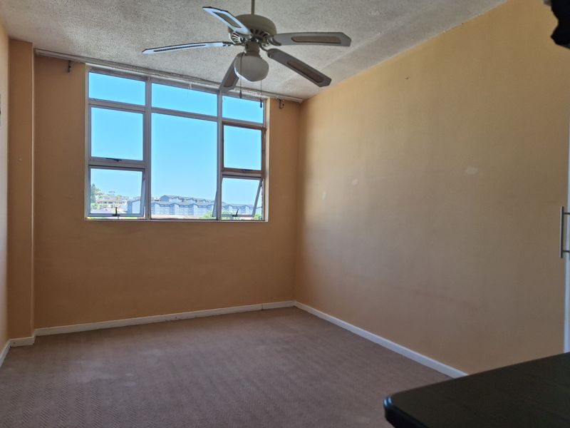 An empty bedroom featuring a ceiling fan, large aluminium windows, and carpeted flooring, offering a blank canvas for potential renovation and interior design updates.