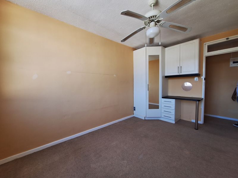 A vacant bedroom featuring a built-in wardrobe, integrated desk unit, ceiling fan, and carpeted flooring, offering a blank canvas for renovation.