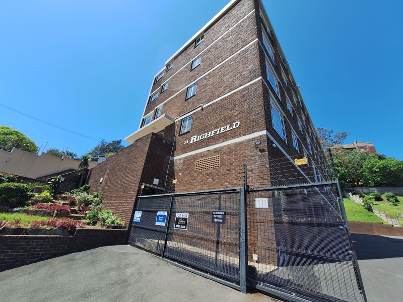 Exterior view of the Richfield apartment building featuring a brick facade, secure gated entrance, and landscaped retaining walls.
