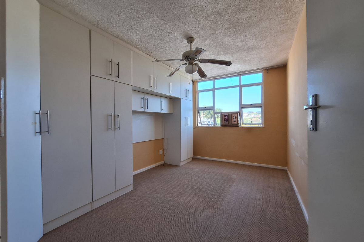 A spacious bedroom featuring extensive built-in cabinetry, a ceiling fan, and large windows that provide natural light and views.