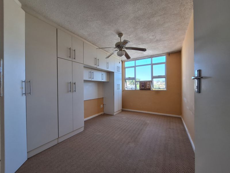 A spacious bedroom featuring extensive built-in cabinetry, a ceiling fan, and large windows that provide natural light and views.
