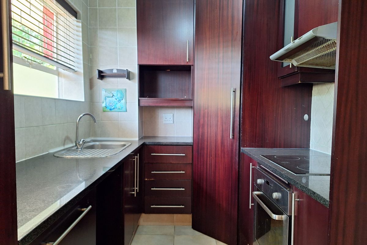 A compact kitchen featuring dark wood cabinetry, granite countertops, built-in oven, electric hob, and tiled finishes.