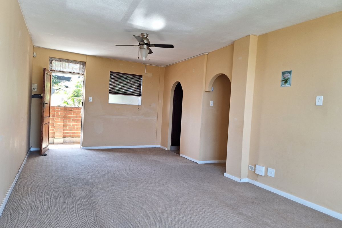 An empty living room featuring carpet flooring, a ceiling fan, and an archway leading to other areas, with direct access to an outdoor space.