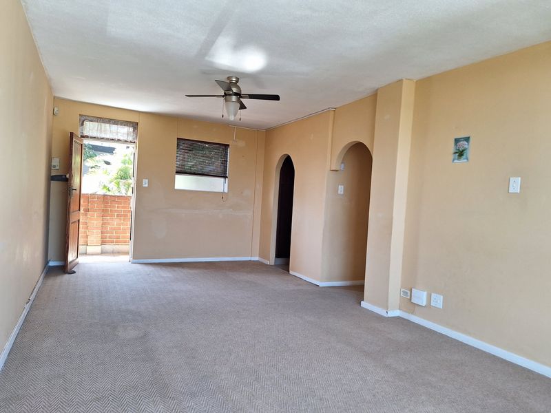 An empty living room featuring carpet flooring, a ceiling fan, and an archway leading to other areas, with direct access to an outdoor space.